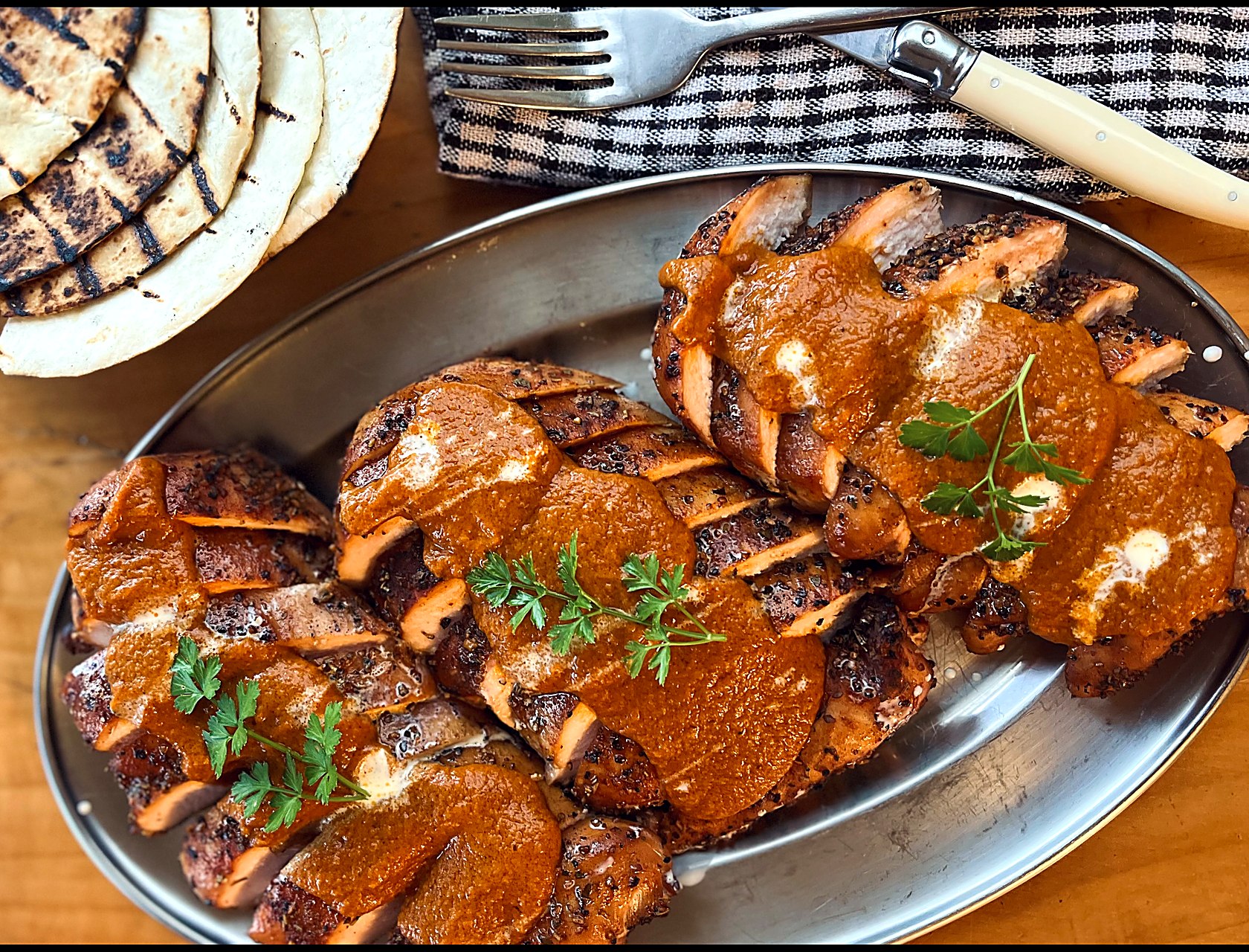 Sliced tikka masala chicken with curry sauce and fresh herbs, grilled flatbreads alongside